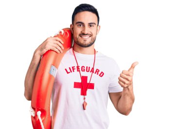 Cankurtaran üniforması giyen genç yakışıklı elinde şamandıra, mutlu ve olumlu gülümsüyor, başparmağıyla mükemmel ve onay işareti yapıyor. 