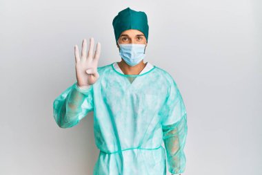 Cerrah üniforması giyen ve tıbbi maske takan genç yakışıklı dört numarayı gösterip işaret ederken kendinden emin ve mutlu bir şekilde gülümsüyor.. 