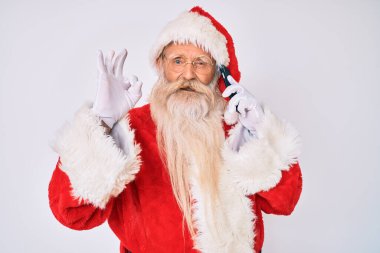 Noel Baba kostümü giyen yaşlı adam telefonda konuşuyor. Parmaklarıyla imza atıyor, gülümsüyor ve mükemmel bir sembol oluşturuyor. 