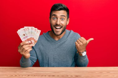 Yakışıklı İspanyol adam elinde Kolombiya pezosu başparmağını kaldırmış, ağzı açık gülümsüyor. 