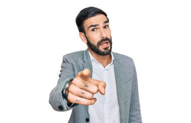 İş kıyafetleri giymiş genç İspanyol bir adam kameraya kızgın ve sinirli bir şekilde seni işaret ediyor. 