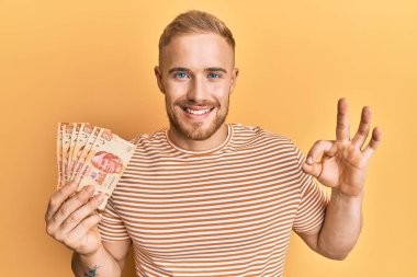 Kafkas asıllı genç adam Meksika pezosu tutuyor. Parmaklarıyla imza atıyor, gülümseyerek mükemmel bir sembol oluşturuyor. 