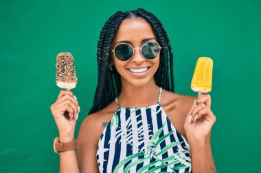 Genç Afrikalı Amerikalı kadın gülümseyerek şehirde dondurma yiyor..