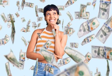 Kısa saçlı, kısa saçlı, rahat giyinen, kameraya kendinden emin, kolları çapraz ve çenesi açık gülümseyen genç esmer kadın. Olumlu düşünmek.