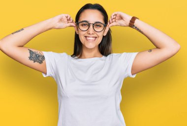 Günlük beyaz tişört giyen genç İspanyol kadın gülümsüyor kulakları parmaklarıyla çekiyor, komik bir jest. deneme sorunu 