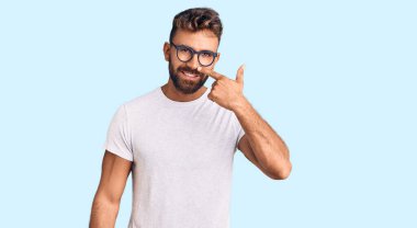 Gündelik kıyafetler giyen ve gözlüklü genç İspanyol adam el ve burun parmaklarıyla işaret ediyor, neşeyle gülümsüyor. güzellik konsepti 