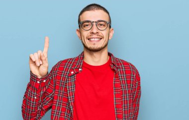 İspanyol genç adam gündelik kıyafetler giyip bir numarayı gösterip işaret ederken kendinden emin ve mutlu gülümsüyor.. 