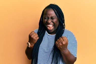 Saçları örgülü genç siyahi bir kadın kolları havada ve gözleri kapalı bir şekilde başarıyı kutluyor. 