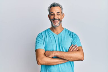 Orta yaşlı, gri saçlı, sıradan kıyafetler giyen mutlu yüzlü, kollarını kavuşturup kameraya bakan bir adam. pozitif kişi. 