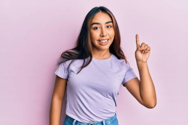 Gündelik kıyafetler giyen genç Latin kadın bir fikir veya soruyla gülümsüyor ve mutlu bir yüzle işaret ediyor. 