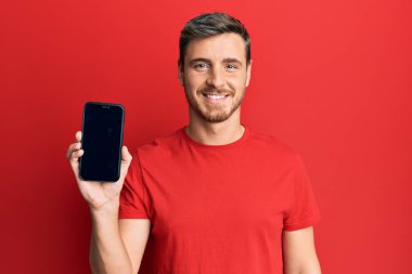 Akıllı telefon tutan yakışıklı beyaz adam ekranda pozitif görünüyor ve mutlu görünüyor. Kendine güvenen bir gülümsemeyle dişlerini gösteriyor. 