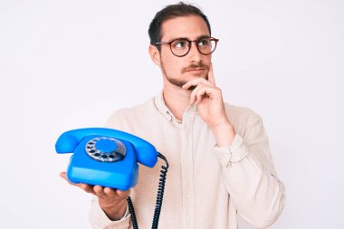 Elinde klasik bir telefon tutan yakışıklı adam ciddi bir yüz ifadesi olan eli çenesinde soru soran, kafa karıştırıcı bir fikir hakkında düşünceli bir adam. 