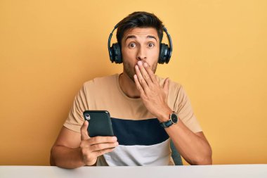 Akıllı telefon takan, ağzı ağızla kapatan ve hata yapmaktan korkan genç, yakışıklı bir adam. şaşırmış ifade 