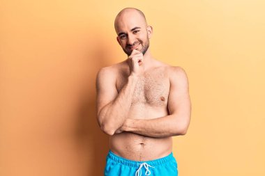 Mayo giyen genç, kel ve yakışıklı bir adam kameraya kollarını kavuşturup çenesini kapatarak gülümsüyor. Olumlu düşünmek. 