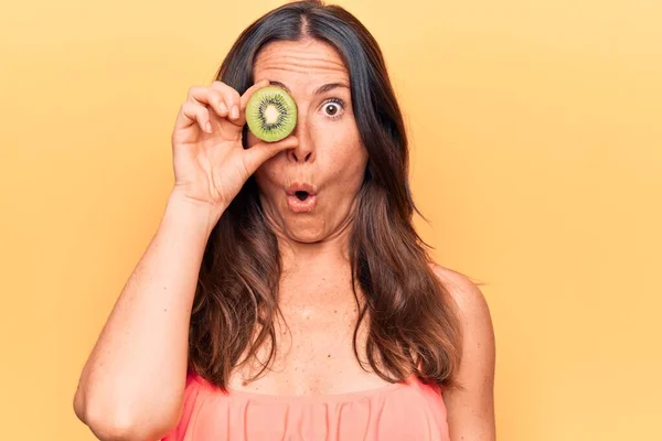 Young Beautiful Brunette Woman Holding Slice Kiwi Eye Isolated Yellow — Stock Photo, Image