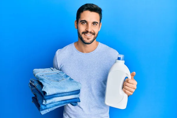 Joven Hombre Hispano Sosteniendo Pantalones Vaqueros Doblados Botella Detergente Sonriendo — Foto de Stock