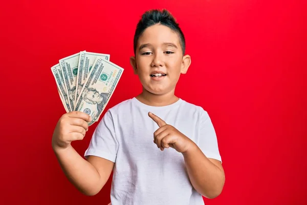 Маленький Мальчик Латиноамериканец Держит Банкноты Долларов Улыбаясь Показывая Пальцем Рукой — стоковое фото