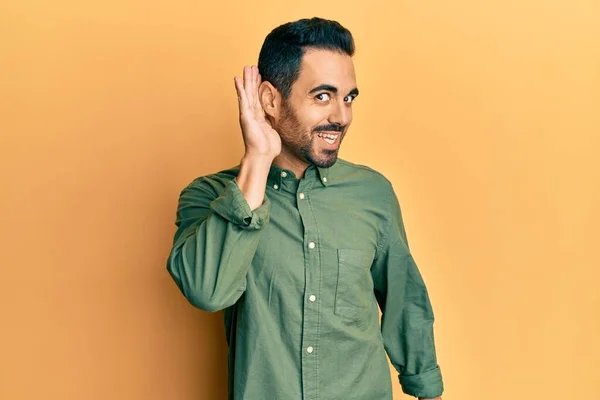 若いヒスパニック系の男が耳を傾け 噂やゴシップに耳を傾け手で笑みを浮かべてカジュアルな服を着て 聴覚障害の概念 — ストック写真
