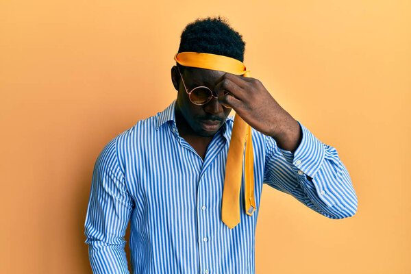 Handsome black man drunk wearing tie over head and sunglasses tired rubbing nose and eyes feeling fatigue and headache. stress and frustration concept.