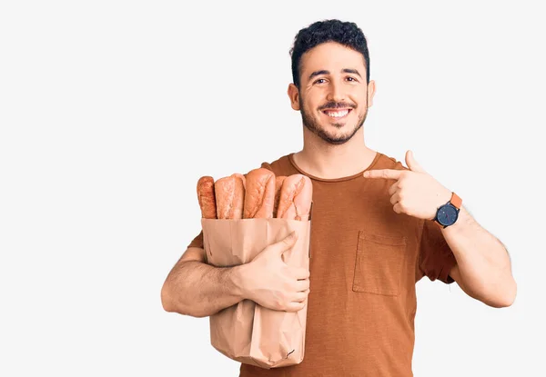 Jovem Hispânico Homem Segurando Saco Papel Com Pão Apontando Dedo — Fotografia de Stock