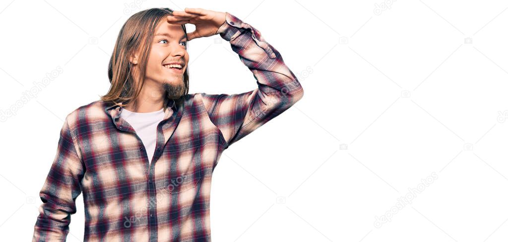 Handsome caucasian man with long hair wearing hipster shirt very happy and smiling looking far away with hand over head. searching concept. 