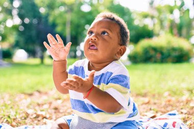 Sevimli Afro-Amerikan tombul çocuk parkta çimlerin üzerinde oturuyor..