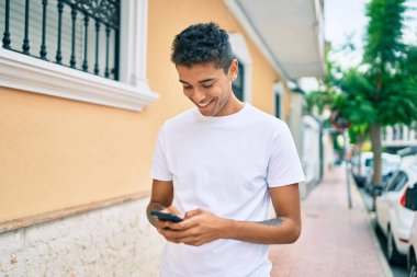Genç Latin adam mutlu bir şekilde gülümsüyor ve şehirde akıllı telefon kullanıyor..