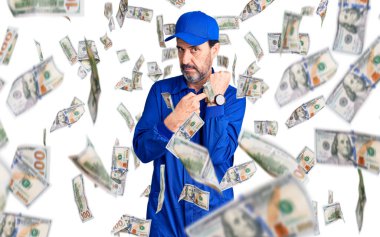 Orta yaşlı, tamirci üniforması giyen yakışıklı adam saati, sabırsızlığı ve rahat bir ifadeyle kameraya bakmayı işaret ediyor.