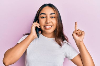 Genç Latin bir kadın akıllı telefondan konuşuyor bir fikir veya soruyla gülümsüyor ve mutlu bir yüzle işaret ediyor. 