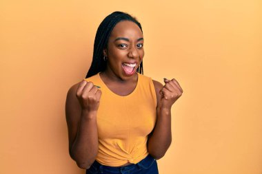 Genç Afrikalı Amerikalı kadın gündelik giysiler giyip kollarını kaldırarak ve açık gözlerle başarıyı kutluyor. Kazanan konsept. 