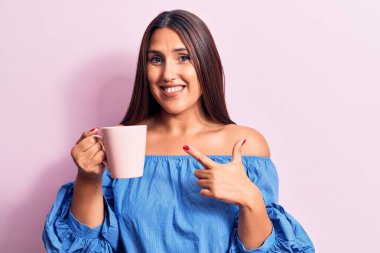 Genç, güzel, esmer kadın kahve fincanı içiyor. Gülümsüyor, mutlu bir şekilde işaret ediyor. 