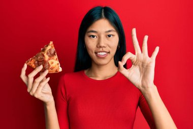 İtalyan pizzası tutan genç Çinli kadın parmaklarıyla imza atıyor, gülümseyerek mükemmel bir sembol oluşturuyor. 