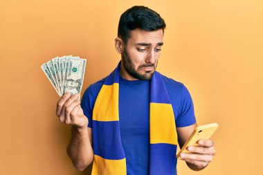 Genç İspanyol futbolcu Amerikan dolarlarını elinde tutan akıllı telefonu kullanıyor. Depresyonda ve endişeli, sinirli ve korkmuş. hüzünlü ifade. 