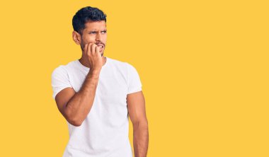 Gündelik kıyafetler giyen genç latin adam gergin ve gergin görünüyor. Ağzı tırnak yiyen ellerle. anksiyete. 