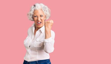 Yaşlı, gri saçlı, günlük kıyafetler giyen kızgın ve kızgın bir kadın öfkeyle bağırırken yumruğunu kaldırıyor. öfke ve agresif konsept. 