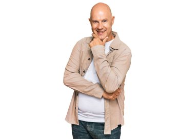 Orta yaşlı kel bir adam, sıradan kıyafetler giyiyor kameraya kendinden emin bakıyor kollarını kavuşturup gülümsüyor ve çenesini kaldırıyor. Olumlu düşünmek. 