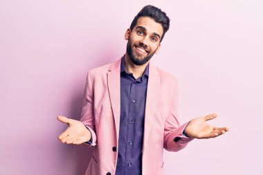 Sakallı, zarif ceketli, kafası karışık, kolları ve elleri havada genç ve yakışıklı bir adam. şüphe kavramı. 