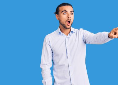 İş kıyafetleri giymiş genç yakışıklı bir adam parmağıyla işaret ederek şaşırmış, ağzı açık, şaşırmış, ön tarafta bir şey var. 