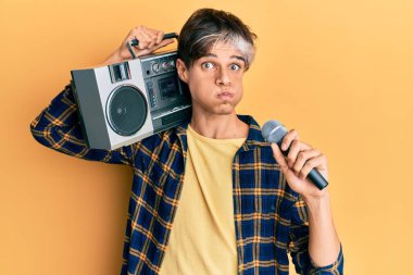 Genç İspanyol adam mikrofon kullanarak şarkı söylüyor ve komik yüzlü yanakları şişiriyor. Ağzı havayla şişer, havayı yakalar.. 