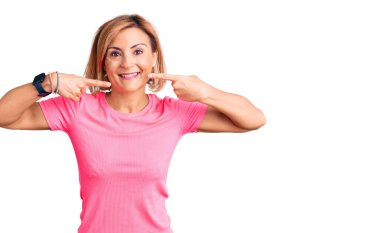 Spor kıyafetleri giyen, neşeli gülümseyen, parmaklarıyla ve ağzıyla işaret eden genç sarışın kadın. diş sağlığı kavramı. 