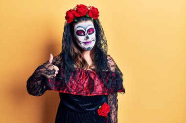 Sarı üzerine ölü kostümü giymiş genç bir kadın elleriyle mutlu bir jest yapıyor. Kameraya bakıp başarıyı gösteren ifade. 