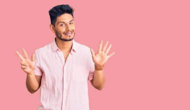 Yakışıklı Latin Amerikalı genç adam rahat bir yaz tişörtü giyiyor ve 8 numaralı parmaklarıyla onu gösterip gülümsüyor.. 