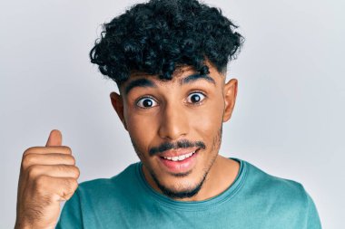 Genç Arap yakışıklı adam gündelik giysiler içinde gururla bağırıyor zaferi ve başarıyı kutluyor kollarını kaldırarak heyecanla bekliyor. 