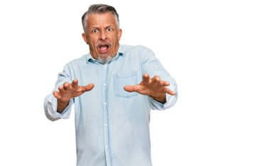 Orta yaşlı, gri saçlı, günlük kıyafetler giyen, korku ifadesinden korkan, dehşete düşmüş, elleri titreyen, şok içinde bağıran bir adam. panik konsepti. 