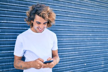 Şehrin caddesinde akıllı telefon kullanan, mutlu gülümseyen genç İspanyol adam.