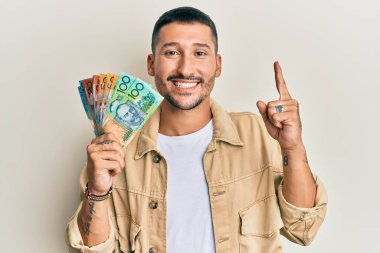 Elinde Avustralya doları olan yakışıklı bir adam bir fikir veya soruyla gülümsüyor ve mutlu bir yüzle işaret ediyor. 