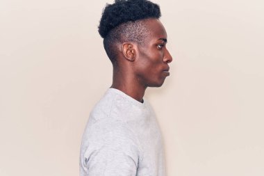 Afro-Amerikalı genç bir adam günlük giysiler giymiş, rahat bir görünüm takınıyor, doğal bir yüz ifadesi ve kendine güvenen bir gülümsemeyle poz veriyor.. 