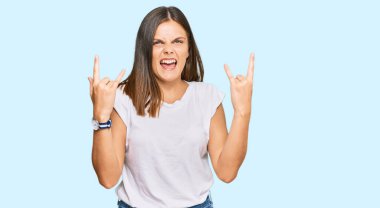 Beyaz gündelik tişört giyen genç beyaz kadın çılgın bir ifadeyle bağırıyor elleri havada rock sembolü yapıyor. Müzik yıldızı. ağır kavram. 