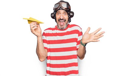 Orta yaşlı havacı, klasik miğfer takmış ve elinde kağıt uçak gözlüğü olan mutlu bir gülümsemeyle başarıyı kutluyor ve kazanan el kaldırarak ifade ediyor.