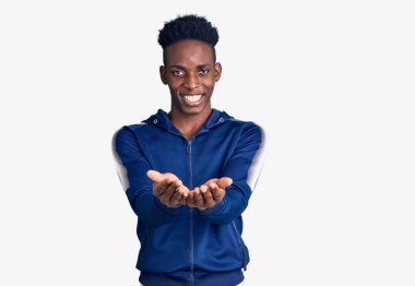 Afrika kökenli Amerikalı genç bir adam spor kıyafetleri giyip avuçlarıyla gülümsüyor ve jest yapıyor. Bekleme ve koruma 